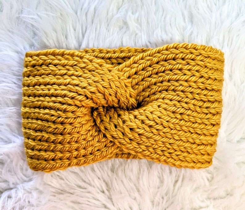 May include: A mustard yellow knitted headband with a knotted design. The headband is made of a soft, chunky yarn.