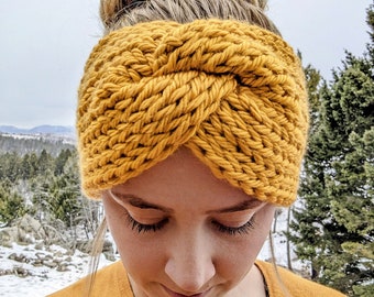May include: A mustard yellow knitted headband with a twisted design. The headband is worn by a person with blonde hair.