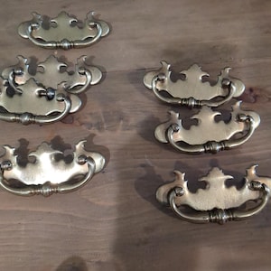 May include: Eight antique brass drawer pulls with a decorative, ornate design. The pulls have a simple, curved handle.