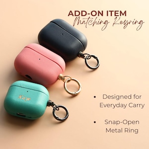May include: Three leather-effect AirPod cases in teal, pink, and navy, each with a metal keyring. The teal case has the name "Kaye" embossed. Text reads "Add-on item Matching Keyring", "Designed for Everyday Carry", and "Snap-Open Metal Ring."