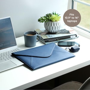 Könnte beinhalten: Eine blaue Laptoptasche mit Klappenverschluss liegt auf einem weißen Schreibtisch neben einem Laptop. Der Text auf dem Bild lautet "Passend für 10,9" bis 16" Laptops". Eine Tasse, Zeitschriften und eine kleine Pflanze befinden sich ebenfalls auf dem Schreibtisch.