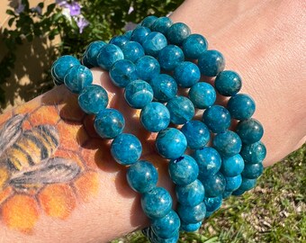 May include: A stack of blue apatite gemstone bracelets. The bracelets are made of round beads and are stacked on a person's wrist.