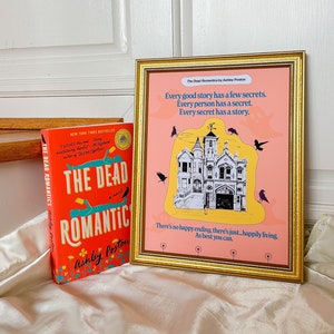 Może przedstawiać: Różowa i żółta okładka książki z tytułem "The Dead Romantics" autorstwa Ashley Poston. Książka leży na białym tle obok oprawionego wydruku z różowym tłem i czarno-białą ilustracją domu. Wydruk zawiera tekst "Every good story has a few secrets. Every person has a secret. Every secret has a story. There's no happy ending, there's just happily living. As best you can."