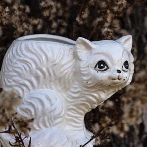 May include: White ceramic cat planter with a fluffy texture. The planter has a wide opening at the top and a small hole at the bottom for drainage.