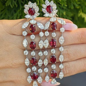 Könnte beinhalten: Ein Paar lange Hängeohrringe mit tiefroten ovalen Rubinen und klaren Diamanten im Marquise- und Rundschliff. Das Design umfasst ein blumenförmiges Oberteil mit einem zentralen Rubin, gefolgt von mehreren kaskadierenden vertikalen Strängen aus abwechselnden Rubinen und Diamanten.
