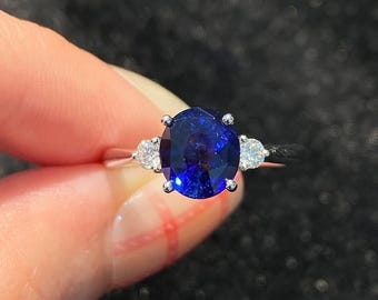 Peut inclure: Une bague à trois pierres avec un grand saphir bleu profond de taille ovale, entouré de deux diamants blancs clairs de taille ronde. Les pierres sont montées sur un anneau en métal argenté poli avec quatre griffes retenant le saphir central.