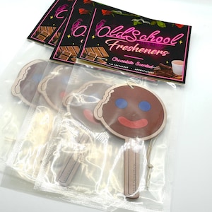 May include: Several air fresheners in clear plastic packaging. The air fresheners are gingerbread man shaped with brown faces, blue eyes, and red smiles. The packaging includes the text "Old School Freshners" and "Chocolate Scented".
