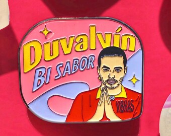 May include: A rectangular enamel pin with a pink background and the words "Duvvalvin Bi Sabor" in yellow and blue. The pin features an illustration of a man in a red shirt with his hands together. The word "Vibras" is on the shirt.