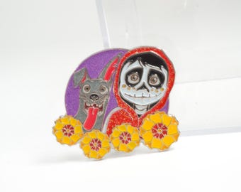May include: Enamel pin featuring a character in a red hoodie with a skull face, a gray dog, and yellow flowers. The pin has a purple background and is set against a white background.