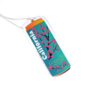 May include: A white car air freshener shaped like a can with a blue and green background. The can has a pink cherry blossom design and the text "California Green Tea and Honey".