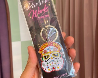May include: A black and white enamel keychain featuring a Stormtrooper helmet with a Day of the Dead sugar skull design. The keychain is attached to a silver key ring and has the text "Storm Vato" and "Parttime Works Since 2018" on the card. The keychain is designed in California.