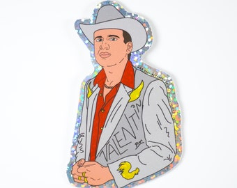 May include: A silver glitter sticker featuring a cartoon illustration of a man wearing a gray suit, red shirt, and a cowboy hat. The man has a mustache and a goatee. The text "VALENTIN" is written on the suit.