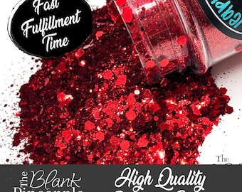 May include: A close-up of a red glitter, with a jar of the glitter spilling out onto a white surface. The jar has a black label with the text "The Blank Pineapple" and "High Quality Polyester Glitter".