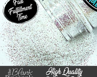 May include: A close-up of a clear jar filled with iridescent white glitter. The glitter is scattered around the jar on a white surface. The text "High Quality Polyester Glitter" is printed on a black banner below the jar. The text "The Blank Pineapple" and a website address are printed on a black banner below the glitter.