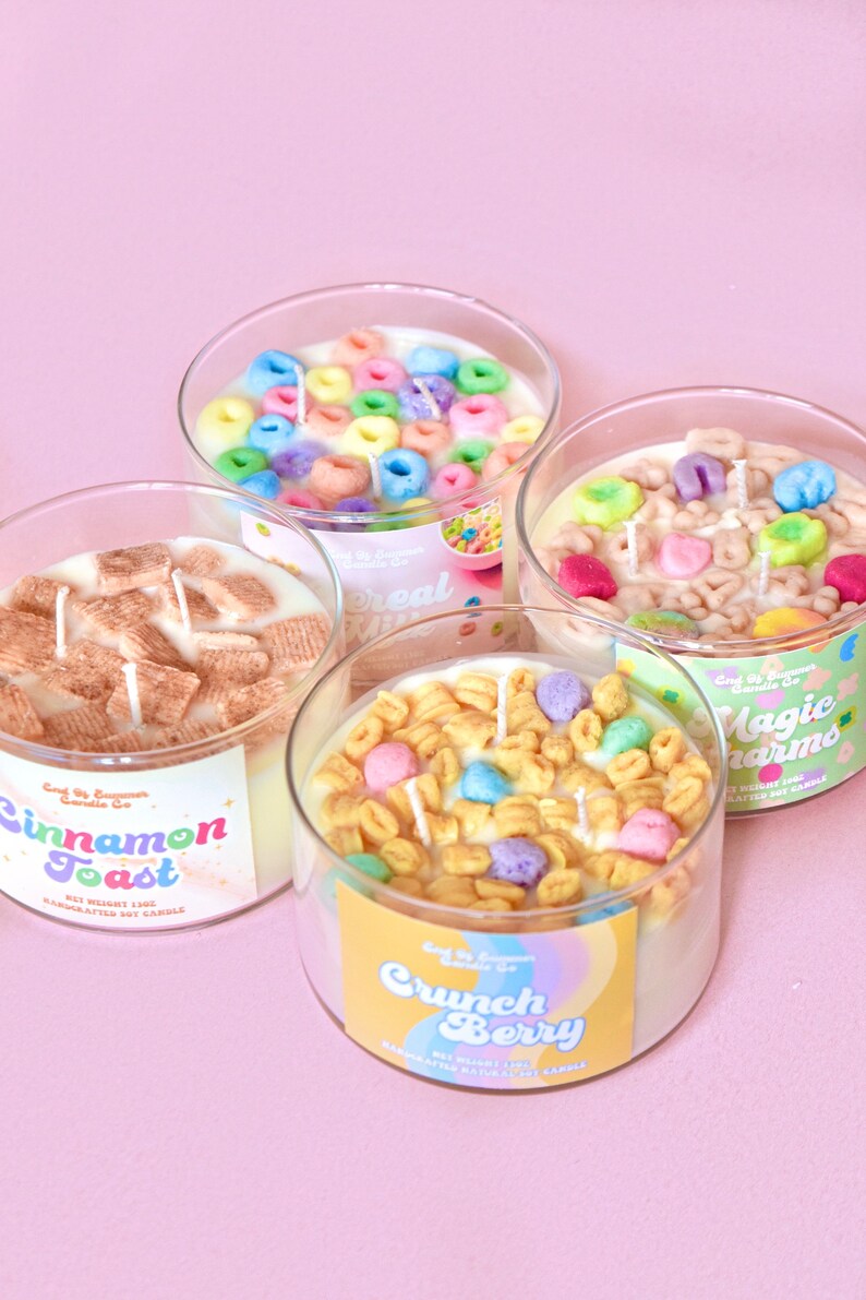 May include: Four glass jars filled with colorful cereal-themed soy candles. The candles are labeled "Cinnamon Toast", "Cereal Milk", "Magic Charms", and "Crunch Berry".