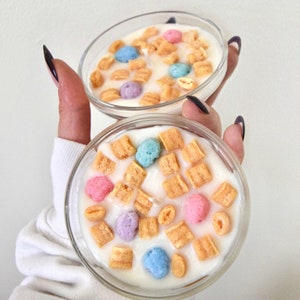 May include: Two clear glass containers filled with a white substance and topped with colorful cereal pieces. The cereal pieces are in the shape of small balls and squares.