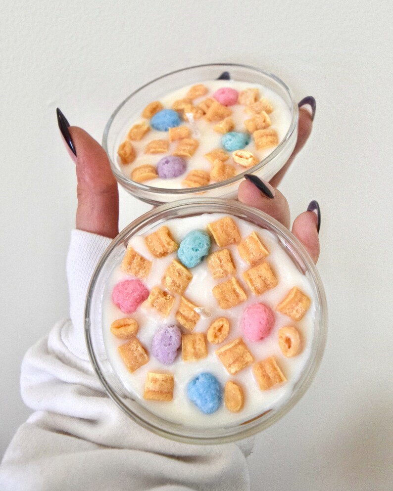 May include: Two clear glass containers filled with a white substance and topped with colorful cereal pieces. The cereal pieces are in the shape of small balls and squares.