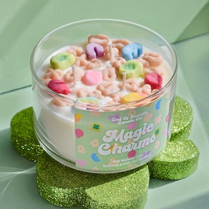 May include: A clear glass jar candle with a white soy wax base and colorful cereal-shaped decorations. The label reads "End of Summer Candle Co. Magic Charms Net Weight 7oz Handcrafted Soy Candle".