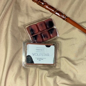 May include: A clear plastic container with a red and black wax melt inside. The wax melt is in the shape of six squares. The container has a label that says "Wolfstar" and "Creations by IH". The label also says "Net Wt. 1 oz."