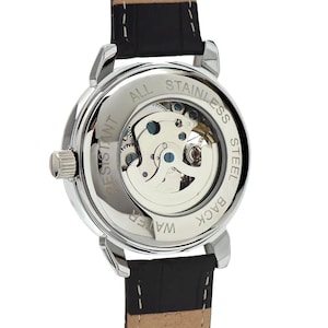May include: Close-up of a silver-toned watch with a black leather band. The watch back is transparent, revealing the inner workings. The words "ALL STAINLESS STEEL", "WATER RESISTANT", and "BACK" are visible.