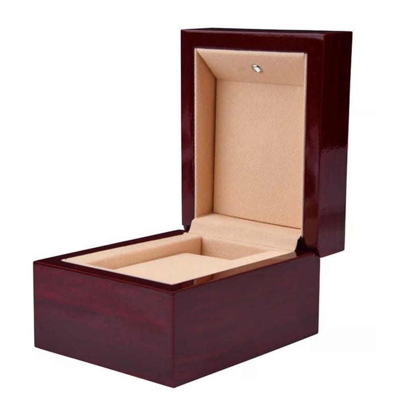 May include: A rectangular, open watch box with a glossy, dark red finish. The interior is lined with a tan, plush material. The box is designed to hold a single watch and has a small light fixture inside.