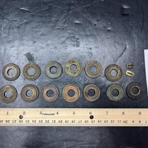 May include: A collection of antique bronze washers and small metal pieces. A wooden ruler with inch markings is placed below the washers. A white label with the number "4084" is also present.