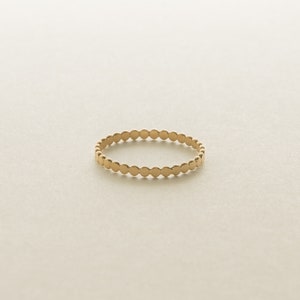 May include: A gold-colored ring with a repeating dot design. The ring is circular and appears to be made of metal. The dots are evenly spaced around the band, creating a textured appearance. The ring is set against a neutral background.