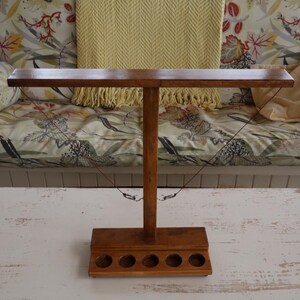 May include: A wooden stand with six round holes and a horizontal bar on top. The stand is made of dark brown wood and has a rustic look.