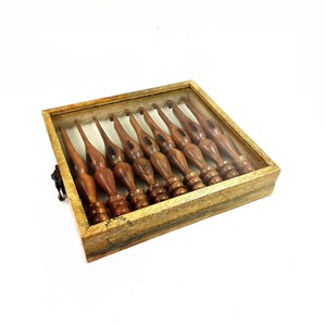 May include: A set of ten wooden crochet hooks in a wooden box with a clear lid. The hooks are arranged in a row and are all the same size. The box is made of dark wood with a light wood trim. The box has a small metal latch on the side.