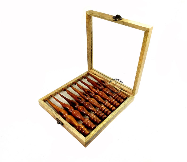 May include: A set of eight wooden crochet hooks in a wooden box with a glass lid. The hooks are different sizes and are arranged in the box in order of size. The box is made of light wood and has a brass latch.
