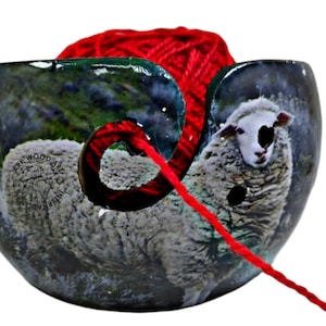 May include: A ceramic yarn bowl with a sheep design and a red yarn ball. The bowl has a hole for the yarn to feed through. The bowl is decorated with the text "Ark Wood Art International".