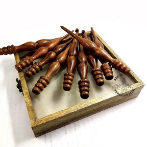 May include: A set of ten wooden knitting needles in a wooden box. The needles are brown and have a pointed tip. The box is made of light brown wood and has a clear glass top.