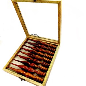 May include: A set of eight wooden crochet hooks in a wooden box with a glass lid. The hooks are different sizes and have a brown finish.