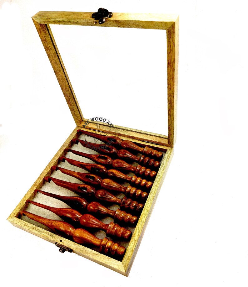 May include: A set of eight wooden crochet hooks in a wooden box with a glass lid. The hooks are different sizes and have a brown finish.
