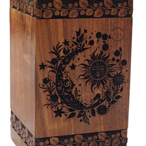 Puede incluir: Una caja de madera con un diseño tallado de un sol y una luna con un patrón floral. La caja es de color marrón oscuro y tiene un acabado de madera natural.