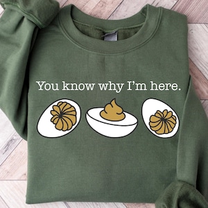 May include: A green sweatshirt with the text "You know why I'm here." and three illustrated deviled eggs.
