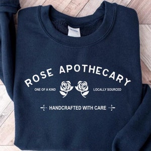 Puede incluir: Sudadera azul marino con texto blanco que dice "Rose Apothecary" con dos rosas blancas y el texto "One of a Kind" y "Locally Sourced". El texto "Handcrafted with Care" tambi&eacute;n est&aacute; impreso en blanco.