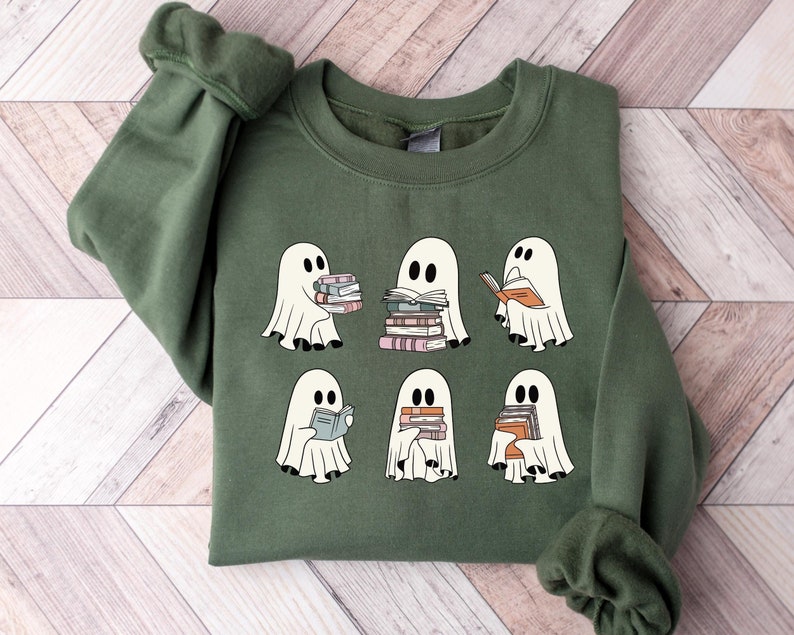 May include: A green sweatshirt with a graphic of six ghosts reading books. The ghosts are white and have black eyes. The books are stacked and have different colors.