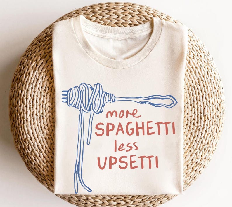 May include: A white t-shirt with a blue and red graphic of a fork with spaghetti on it. The text "more spaghetti less upsetti" is written in red and blue.