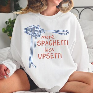May include: White sweatshirt with a blue and red graphic of a fork with spaghetti and the text "more spaghetti less upsetti".