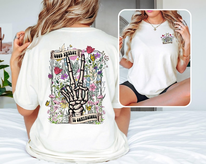 May include: White t-shirt with a floral design and a skeleton hand making a peace sign. The text "Good Energy is Contagious" is printed on the shirt.