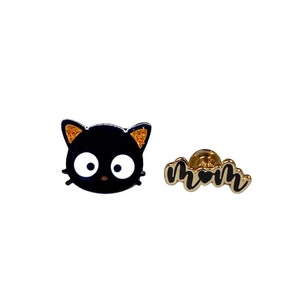 May include: A pair of gold-tone enamel pins featuring a black cat with orange ears and the word "mom" with a heart in the middle.