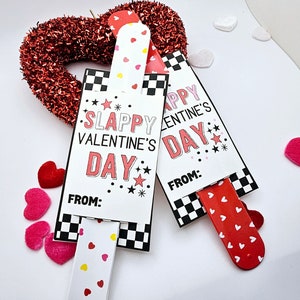 May include: Two Valentine's Day slap bracelets with a black and white checkered design. The bracelets have red and white hearts and the text "Slappy Valentine's Day" and "Happy Valentine's Day".