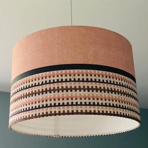 May include: A pink and brown patterned lampshade with a black trim. The lampshade is made of fabric and has a white interior.