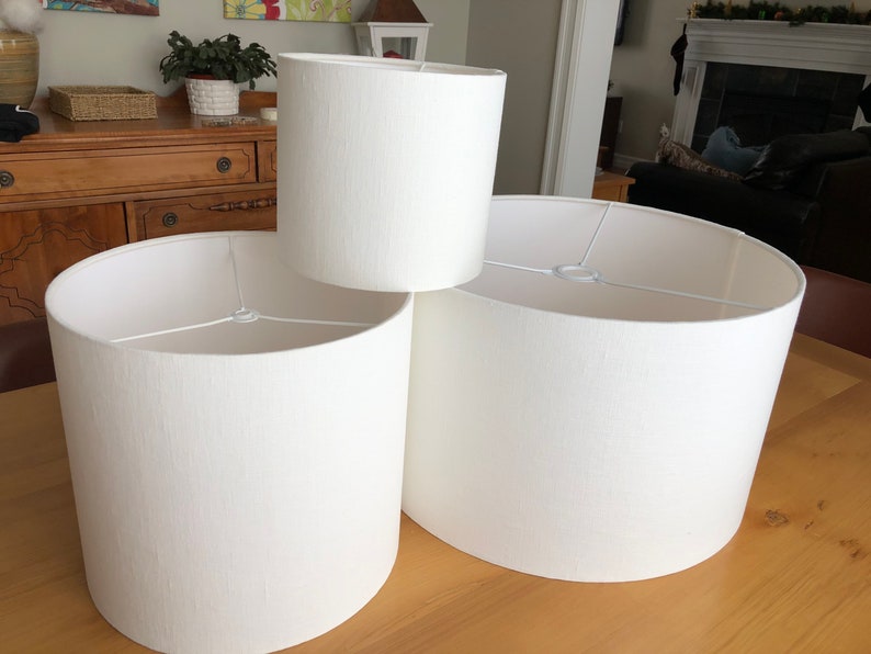 May include: Three white fabric lampshades of different sizes. The lampshades are cylindrical and have a textured surface.