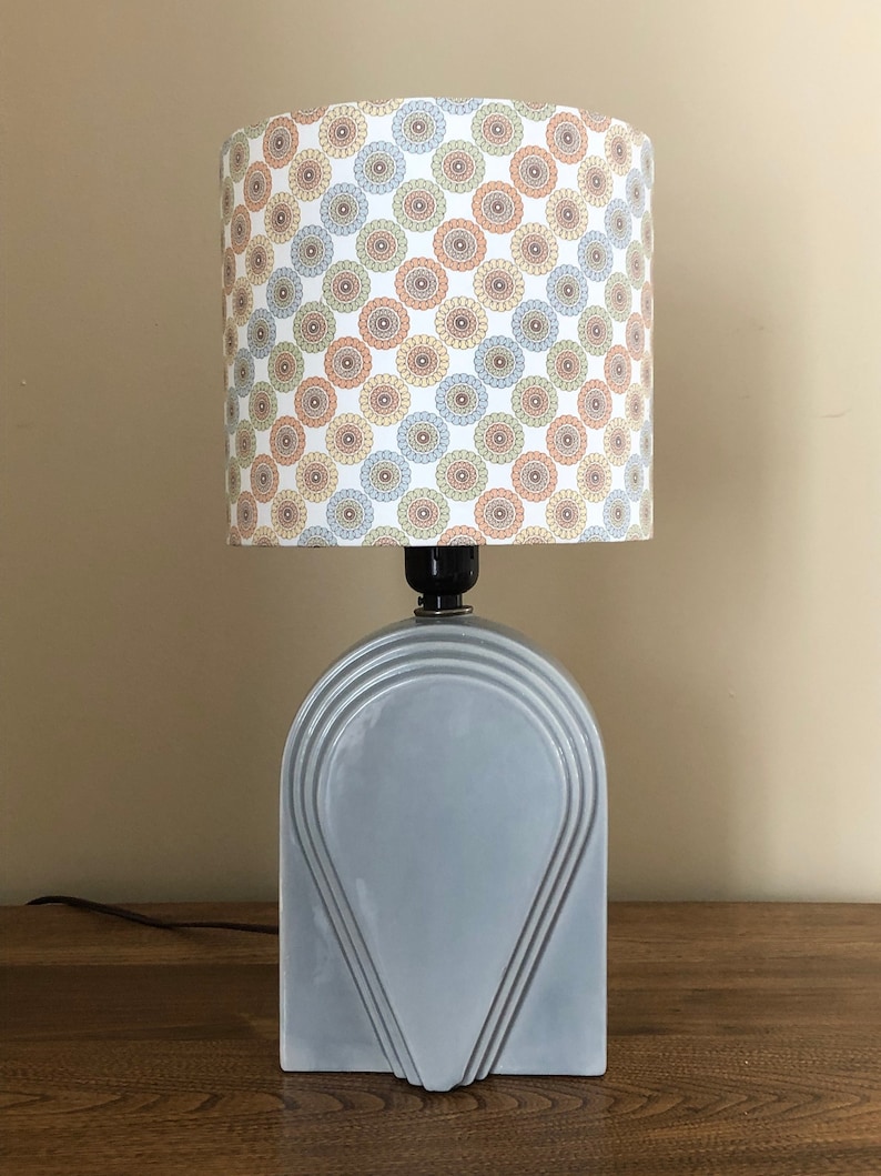 May include: A gray ceramic table lamp with a geometric design. The lampshade is white with a pattern of colorful circles.