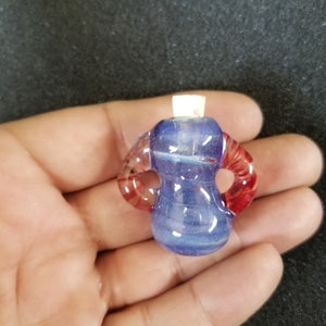 May include: A small, blue glass pendant with red and white swirls. The pendant has two loops on the sides.