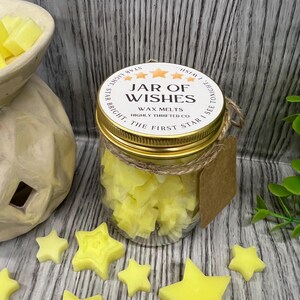 May include: A glass jar filled with yellow star-shaped wax melts. The jar has a gold lid with the text "JAR OF WISHES WAX MELTS HIGHLY THRIFTED CO. STAR BRIGHT, THE FIRST STAR I SEE TONIGHT."