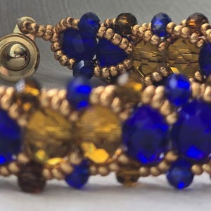 May include: A detailed bracelet with a repeating pattern of blue and amber-coloured faceted beads. The bracelet is embellished with small gold-coloured beads and a gold-coloured clasp. The jewellery is suitable for both everyday wear and special events.