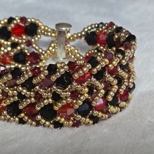 May include: A multi-strand bracelet featuring black, red, and gold beads. The bracelet is woven in an intricate pattern and has a silver clasp.